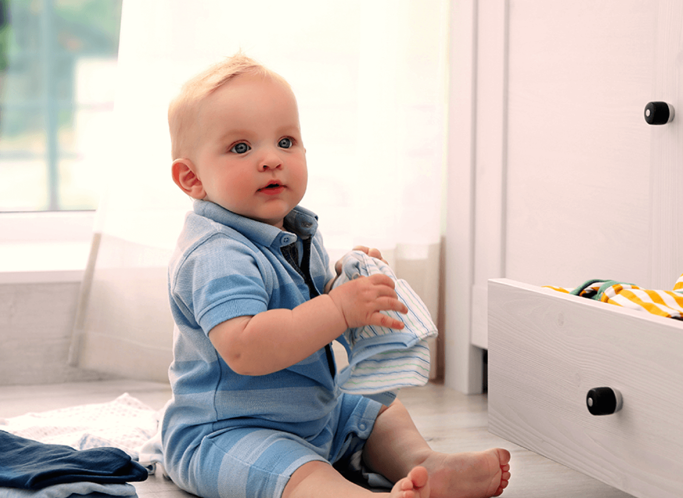 A baby sits on the floor and plays with some laundry. He is looking off camera